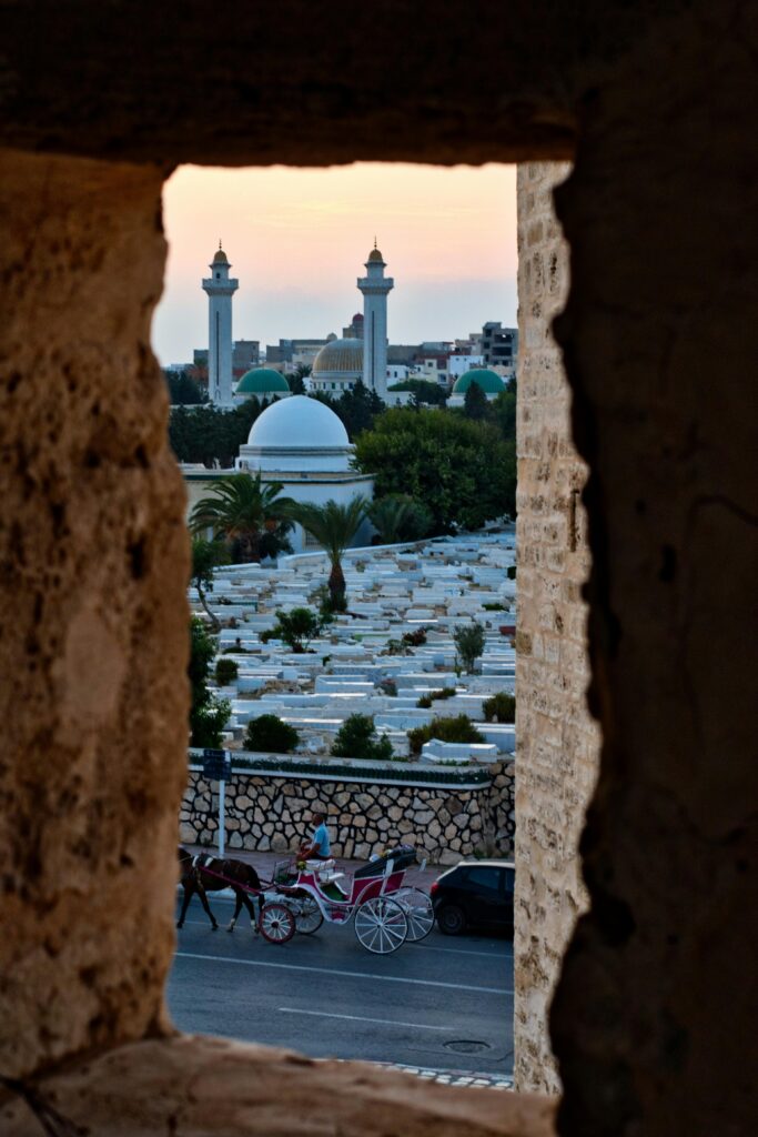 A picturesque view of a mosque with minarets and a horse carriage, framed by an ancient wall at sunset.